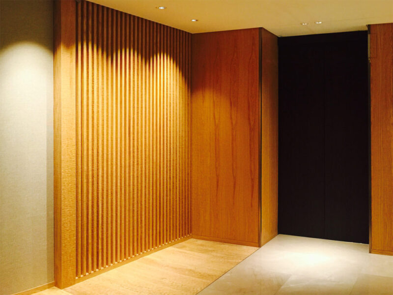 スプーンカット加工のフローリングと縦格子の壁デザインが調和するエレベーターホール