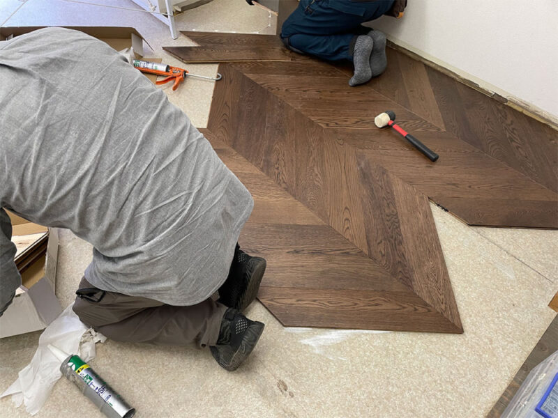 複合フローリングを用いたフレンチヘリンボーン施工風景。職人が角度を調整しながら貼る様子