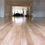 施工後のシルバーチェリー無垢フローリングと奥で仕上げ作業を行う職人