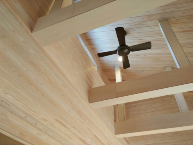 吉野杉羽目板が広がる天井と梁、シーリングファンを備えた吹き抜け空間