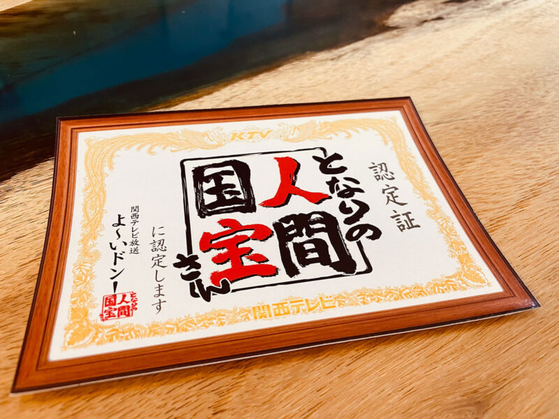 関西テレビ「となりの人間国宝さん」の認定証と木のテーブル