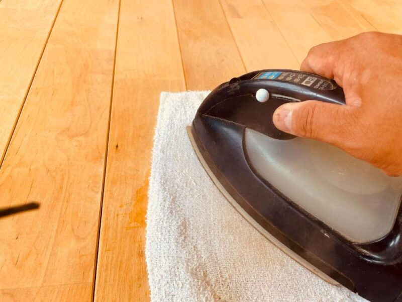 濡れタオルをあててアイロンで無垢フローリングのへこみを補修している様子