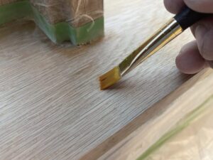 オーク材の鉄染み除去作業中。筆でシュウ酸を塗布し、黒ずみ部分を中和している様子。