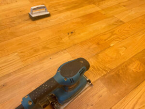 電動サンダーを使って水染みを研磨している無垢フローリングの様子。