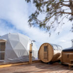 白いドームテントと木製バレルサウナが並ぶデッキスペース