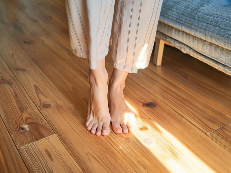 朝日が差し込む室内で、赤松の無垢フローリングの上に立つ人の足元。柔らかな光と木目の温かさが際立つ。
