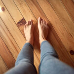 赤松の無垢フローリングの上に裸足で立つ人の足。天然木ならではの暖かさと心地よさが伝わるイメージ。