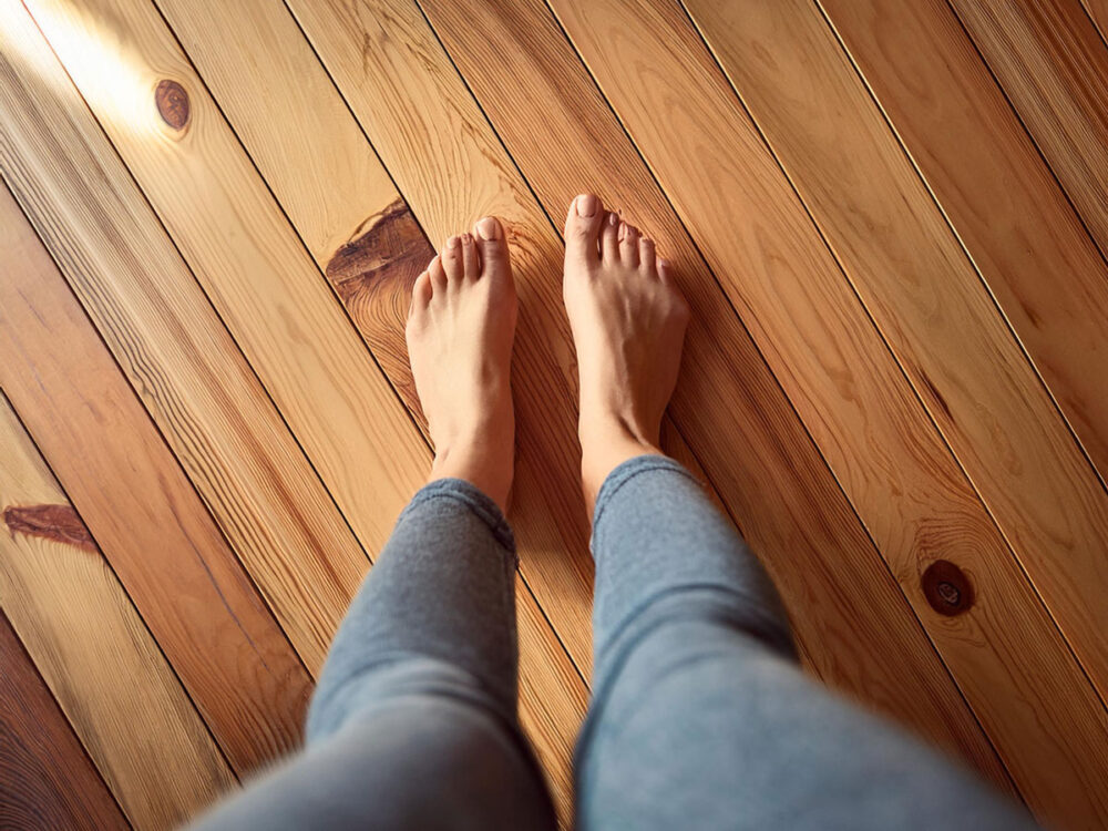 赤松の無垢フローリングの上に裸足で立つ人の足。天然木ならではの暖かさと心地よさが伝わるイメージ。