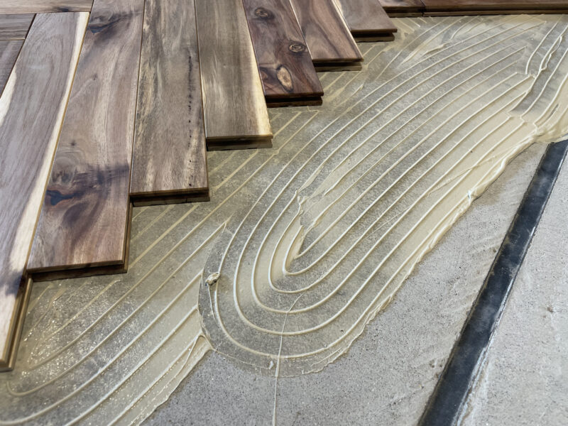 下地に接着剤を塗布して無垢フローリングを直貼り施工している現場写真