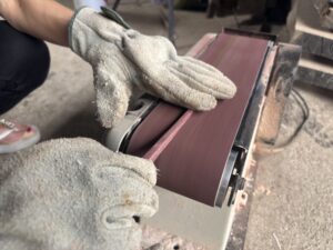 ベルトサンダーで箸先を細く仕上げている手元のアップ