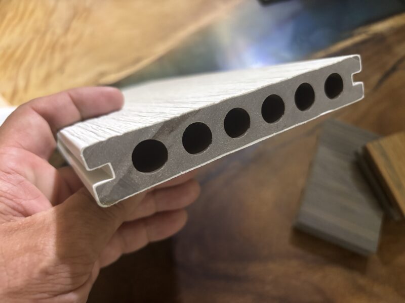 共押出（Co-extruded）人工木デッキの断面構造。中空部を持つ二層構造で、外層には高耐候ポリマーがコーティングされている。