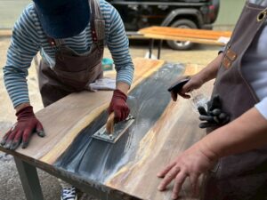 ブラックグレーのレジンを流し込んだ無垢板をコテで研磨する参加者たち