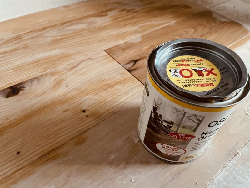 無垢フローリングの上に置かれたオスモカラーの缶と施工前の床材