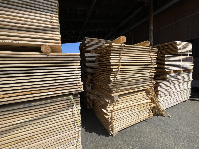 桟木を挟みながら無垢材が整然と積まれ、木口や木肌の質感が近距離でわかる写真。