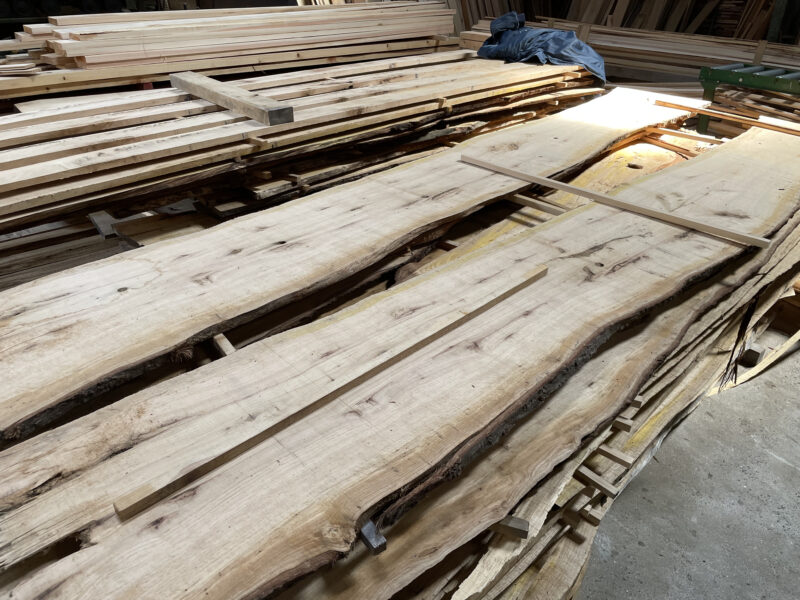 屋根付きの屋外スペースで無垢材が桟積みされ、自然乾燥が行われている様子。