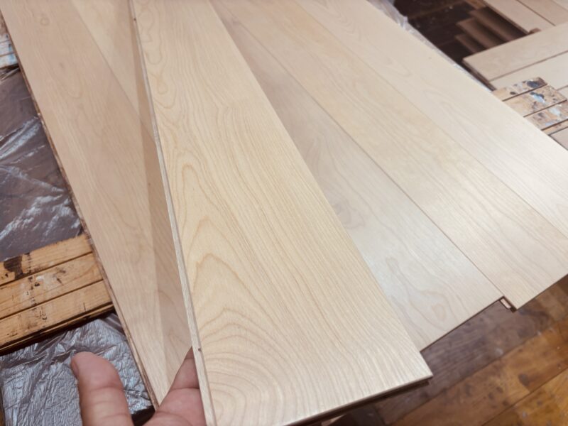 白木仕上げを施したバーチ（カバ / 樺）一枚もの・床暖房対応複合フローリング材を手に持って質感を確認している様子。