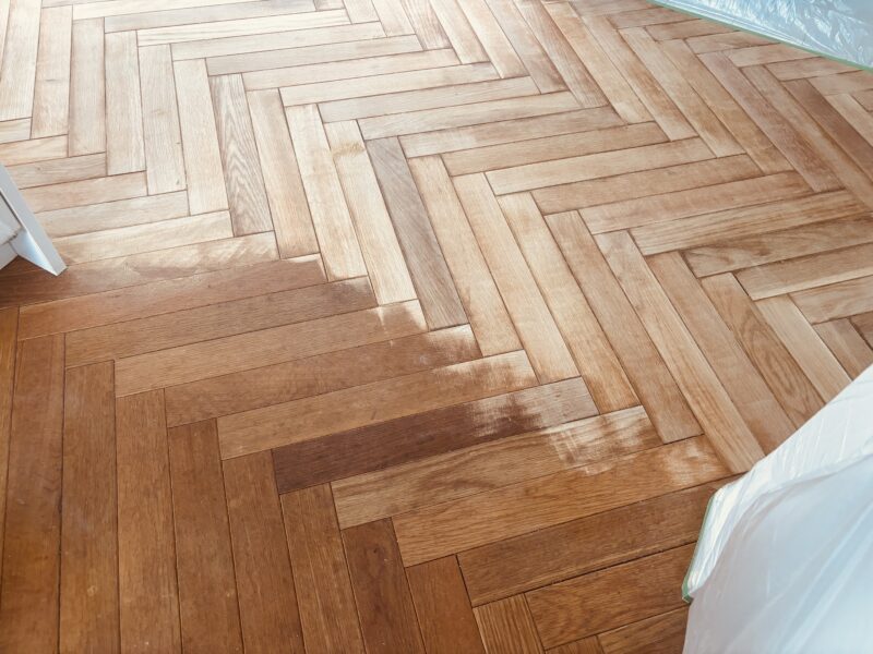 ヘリンボーンフローリングを全面サンディング中。黒ずみが落ちて木目がはっきり現れ始めている。