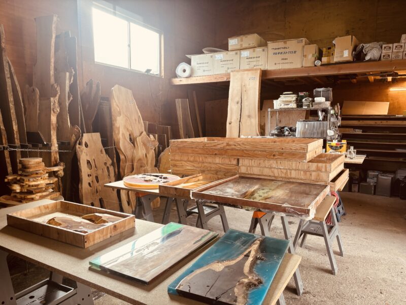 NHKの生放送に向けて片づけ作業が進むエコロキアのアトリエ内部。レジンテーブルの型枠や無垢材のスラブ材が並び、制作途中の作品が作業台に置かれている。