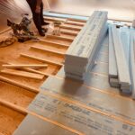 ヒノキ無垢フローリング施工のために、和室でスタイロフォーム断熱材をカットしながら下地を整えている職人の様子。