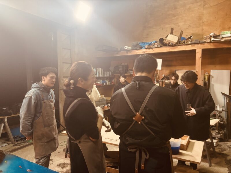 レジンテーブル制作現場で談笑しながら作業に参加するエコロキアのスタッフと仲間たち。温かい雰囲気の中、NHKの撮影準備が進む様子。