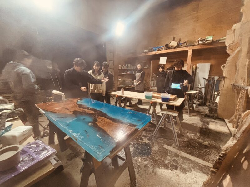 NHK奈良「ならナビ」生放送の撮影が行われているエコロキア御所アトリエ。大型のブルー波レジンテーブルを囲み、スタッフと参加者が準備を進めている様子。