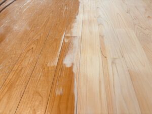 ヒノキ無垢フローリングを研磨して再生している途中の様子。右側は削りたての明るい木肌、左側は経年劣化した古い塗膜が残っている状態。