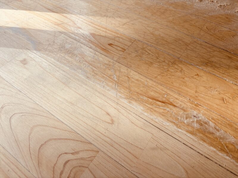 サンダーで研磨されたヒノキ無垢フローリングに木粉が積もった状態。古い塗膜が削られ、新しい木目が出てきている途中工程。