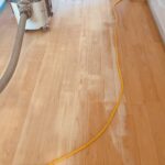 芦屋市の現場でヒノキ無垢フローリングを研磨している様子。研磨機と吸塵ホースが見え、削りたての明るい木肌が現れている
