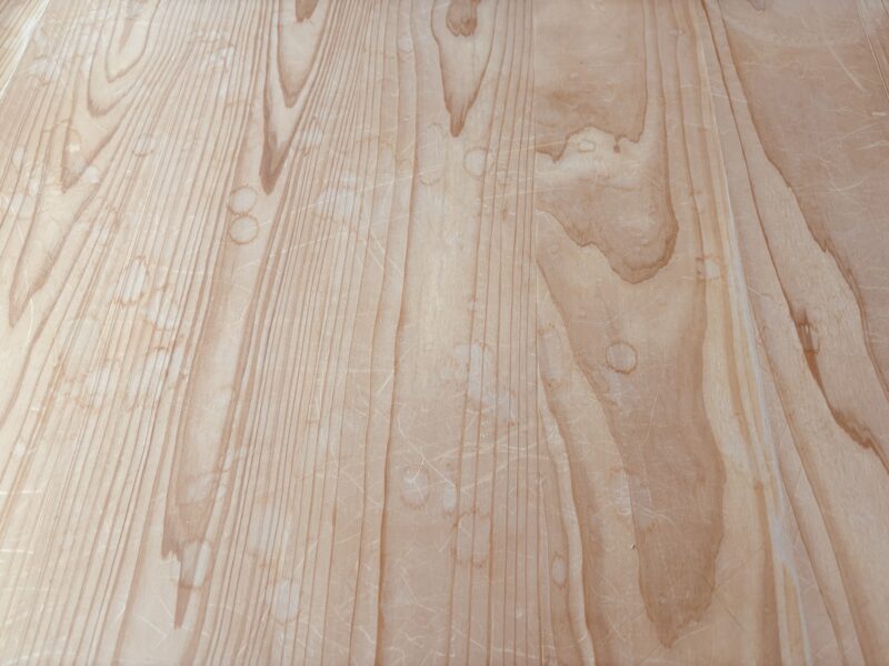 杉フローリング全体に輪じみや細かな傷が多数残り、白濁が広がっている施工前の状態。木目がくすみ、部分的に濃い汚れも見られる。