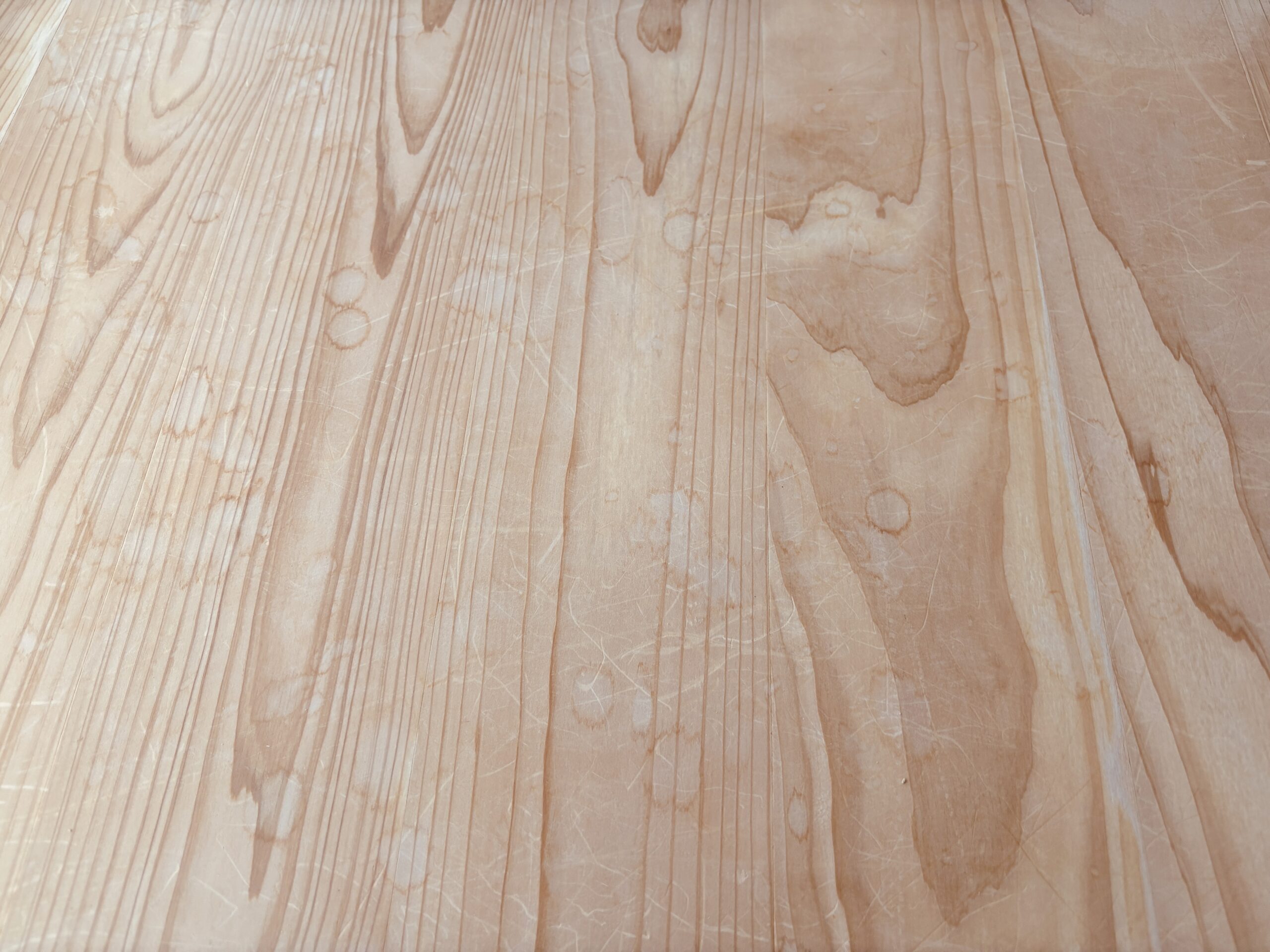 杉フローリング全体に輪じみや細かな傷が多数残り、白濁が広がっている施工前の状態。木目がくすみ、部分的に濃い汚れも見られる。