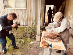 御所市観光振興課の担当者さんがカメラを構え、レジンテーブル制作中の参加者さんを真剣な表情で撮影している様子。