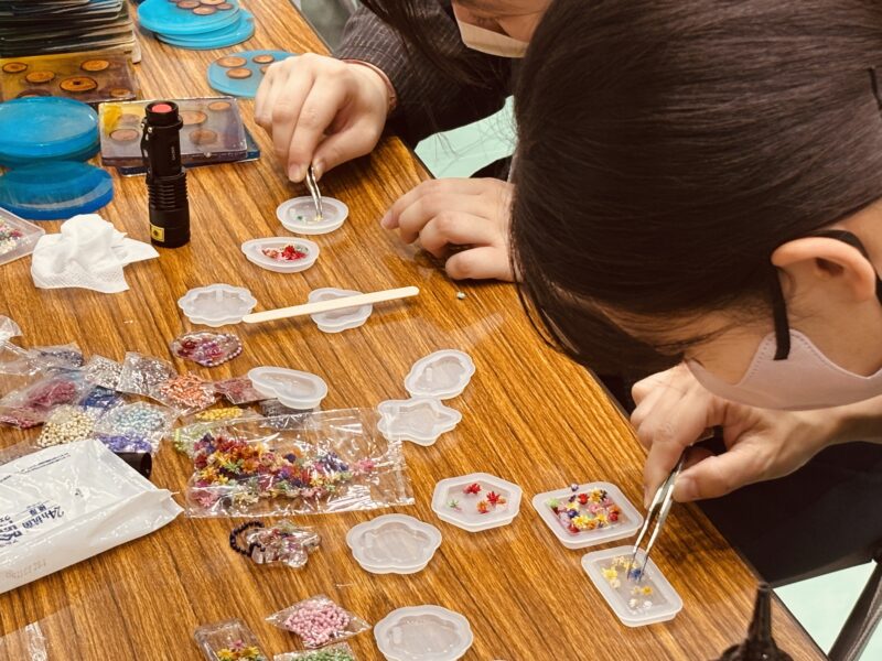 ピンセットで小さな素材を配置し、レジンキーホルダーを制作している手元の様子