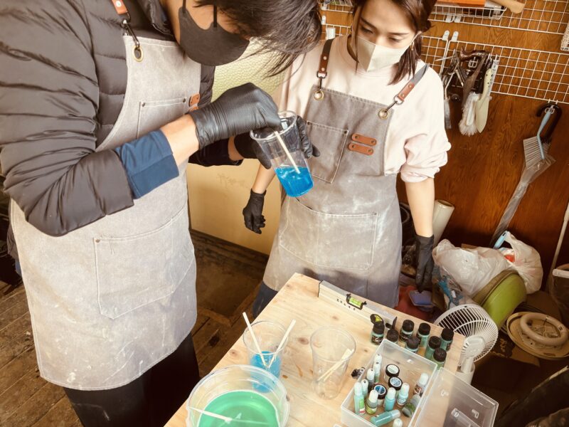 レジンテーブル制作体験ワークショップで、宮古ブルーをイメージした青いレジンに顔料を混ぜるご夫婦