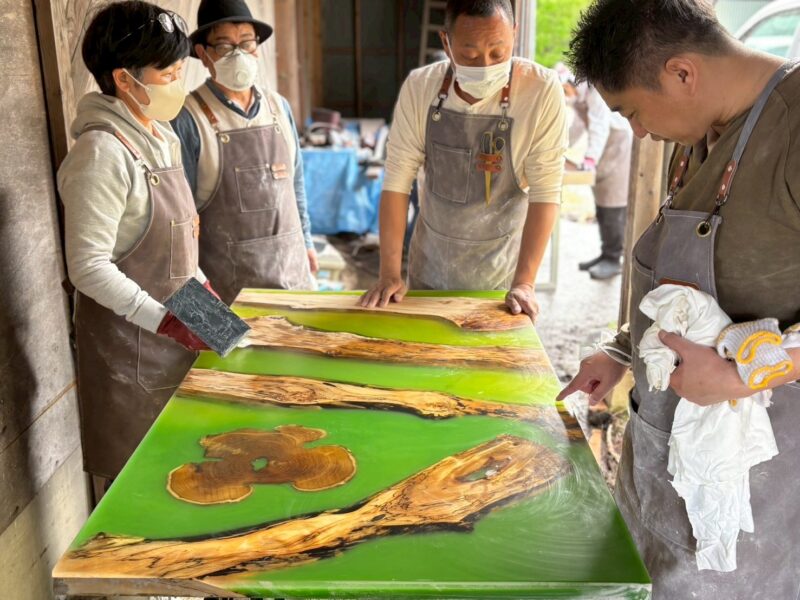 大きなグリーン系レジンテーブルの表面を確認しながら仕上げ作業を行う参加者さんたちの姿。