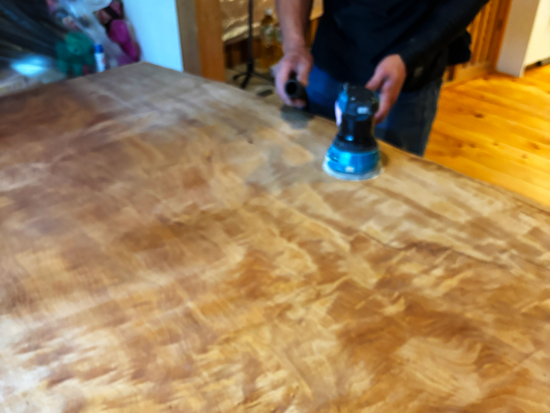 栃の一枚板テーブルをオービタルサンダーで磨き直している作業風景。表面の色ムラを均一に整えている工程。