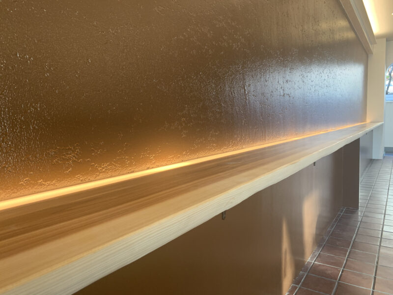 マンションのエントランスに設置された奈良県産吉野杉の無垢カウンター。間接照明に照らされ、木目の美しさが際立つカウンター。