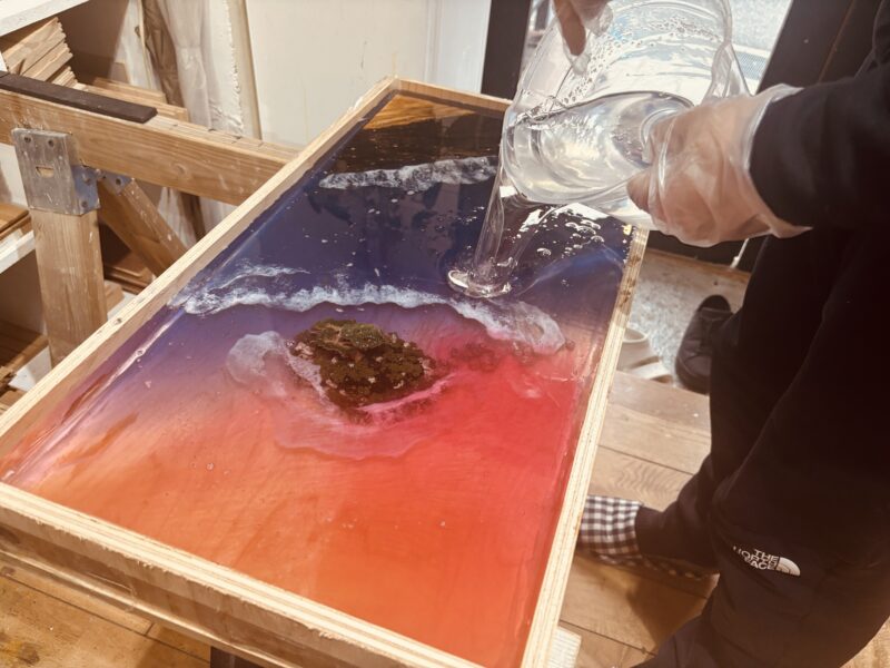 二人で協力しながらレジンテーブルにレジンを流し込んでいる制作体験の様子