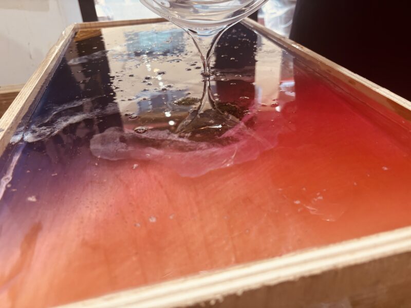 制作途中のレジンテーブルに透明なレジンをゆっくり流し込んでいる様子のクローズアップ