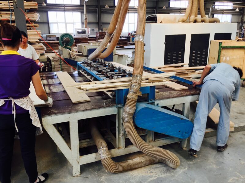 中国の工場で無垢フローリング材を加工する様子。集塵設備のある機械で木材を加工する作業風景。
