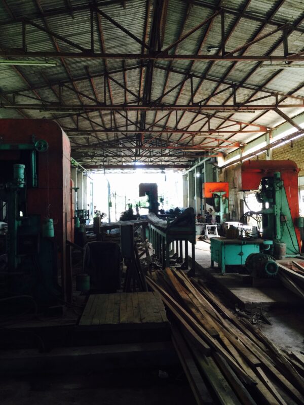 ミャンマーの木材工場で無垢材を加工する現場。大型の木工機械と製材途中の木材が並ぶ工場内の様子。