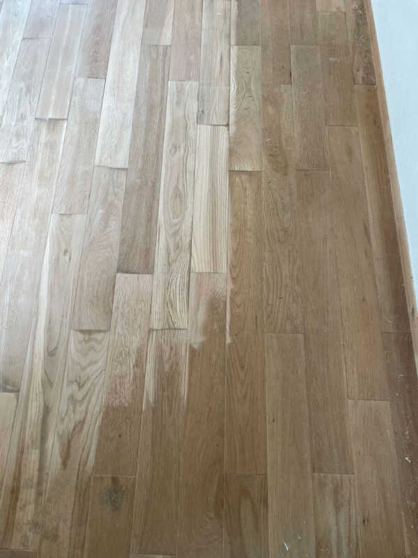 専用機械で研磨中の無垢フローリング。表面塗膜を除去して木地を整えている工程