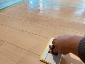 無垢フローリングに自然塗料をヘラで均一に塗布しているメンテナンス作業の様子