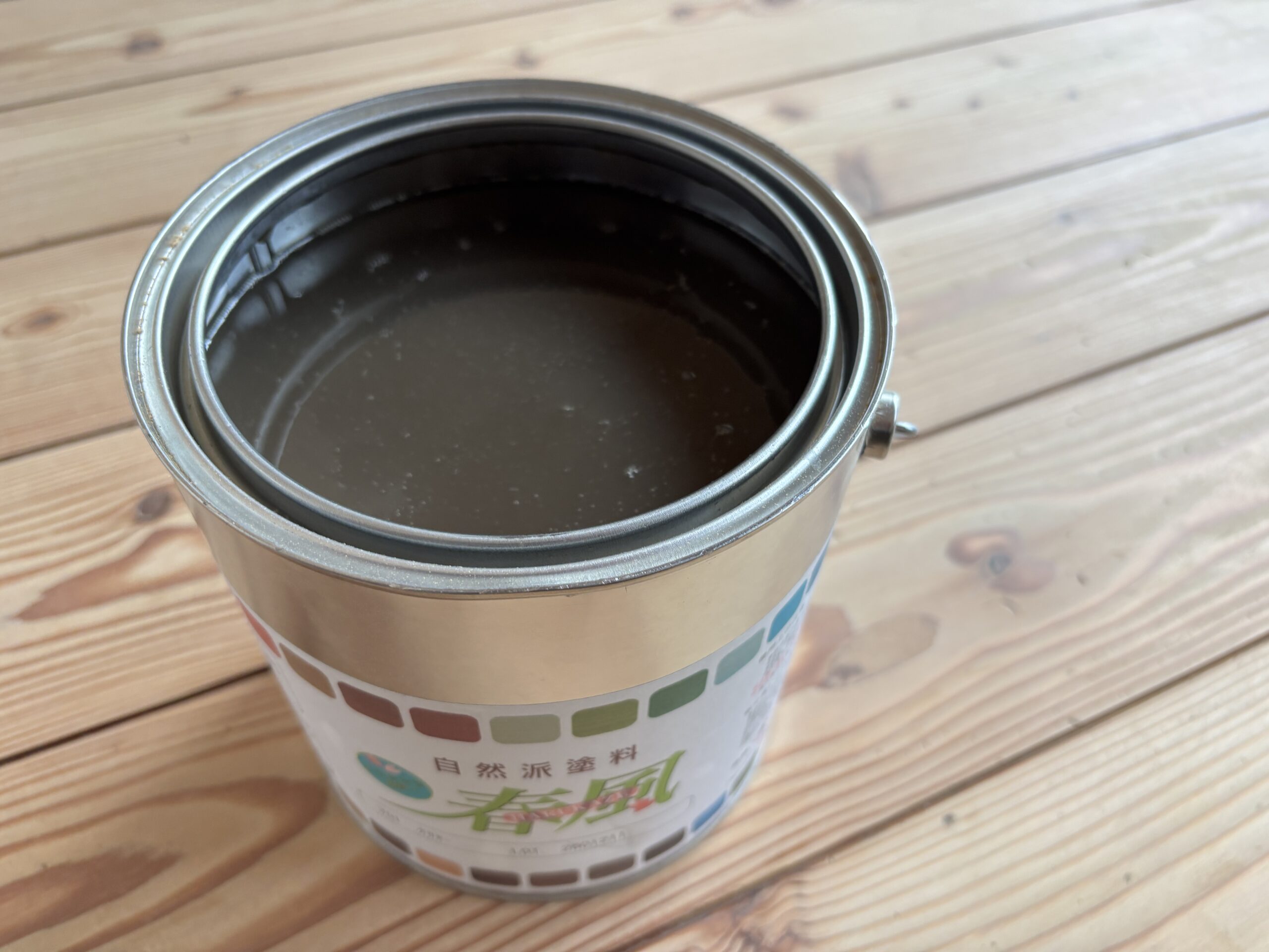 自然塗料「春風」クリアの塗料缶。杉の無垢フローリングの上に置かれた未使用状態の塗料。